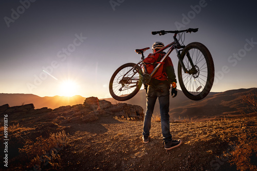 Male mountain biker goes uphill and carry a bicycle on his back to sunset mountain