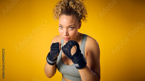 Studio Shot Of Woman Wearing Gym Fitness Clothing In Boxercise Class Sparring On Yellow Background photo
