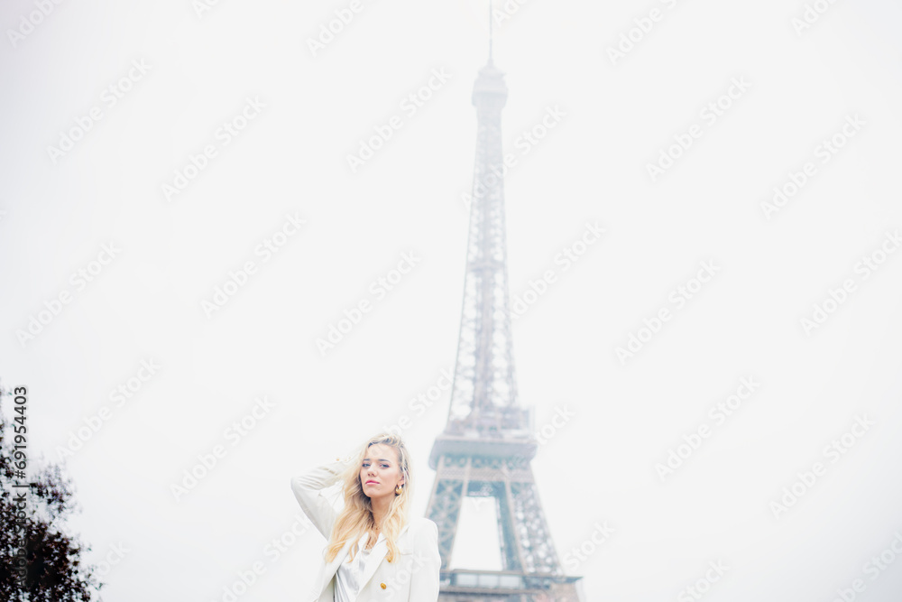 Pretty blonde girl with long hair poses against background of sky and Eiffel Tower.Tourism. 