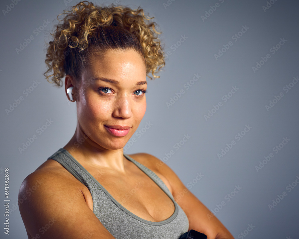Studio Portrait Of Woman In Gym Fitness Clothing Streaming To Wireless Ear Buds From Fitness Tracker Studio Portrait Of Woman In Gym Fitness Clothing Streaming To Wireless Ear Buds From Fitness Tracker