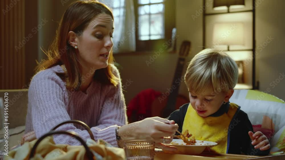 A young mother feeds pasta to her beautiful son, sitting at the dining table, together with the rest of the family. A young mother feeds pasta to her beautiful son, sitting at the dining table, together with the rest of the family.