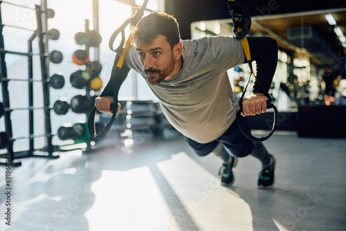 Athletic man using suspension straps while exercising strength in gym. photo