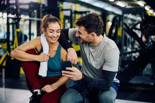 Happy couple of athletes using smart phone in gym.