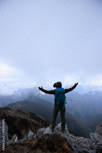 Woman hiker enjoy the view on mountain top cliff edge face the snow capped mountains in tibet