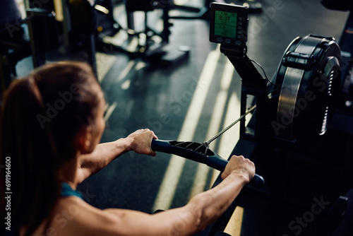 Close up of athletic woman using rowing machine while working out in gym.