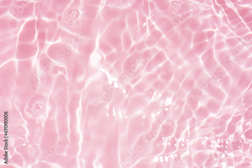 Pink water bubbles on the surface ripples. Defocus blurred transparent pink colored clear calm water surface texture with splash and bubbles. Water waves with shining pattern texture background