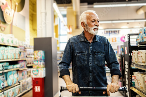 A gray-haired pensioner in a grocery store chooses groceries. Senior customer buying in supermarket. photo