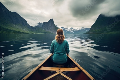  a woman sitting in a boat in the middle of a body of water with a mountain range in the background.