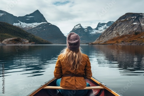  a woman sitting in a boat on a lake with mountains in the background and snow capped peaks in the distance.