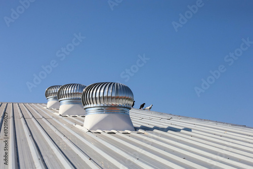 Ventilation fan on the roof. Three shiny metal rotating balls on industrial factory roof for circulating cool air into warehouse on blue sky background with selective focus.