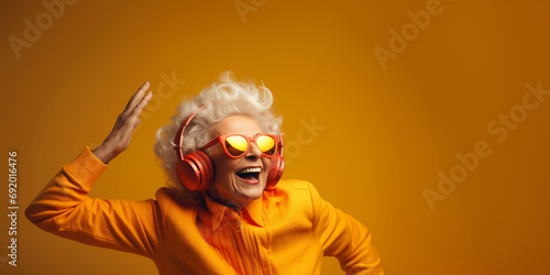 Satisfied old woman with grey hair wearing bright headphones and clothes does best body moves energetically. Cheerful senior woman in bright sunglasses smiles broadly dancing to favourite song