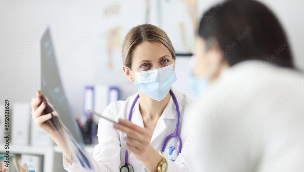 Doctor in protective mask showing patient X ray. Diagnostics of vertebral hernia concept Doctor in protective mask showing patient X ray. Diagnostics of vertebral hernia concept