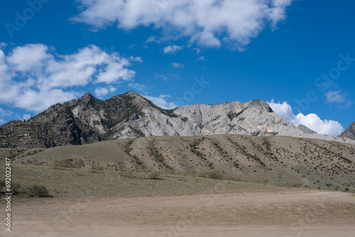A mountain and a hill in the steppe on a sunny day against a background of blue sky with clouds