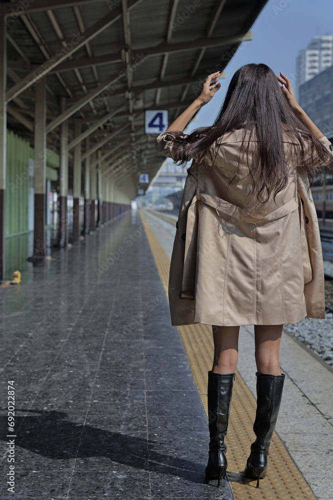 Beautiful Asian woman wearing trench coat stands on a platform near the tracks, hands in her hair Beautiful Asian woman wearing trench coat stands on a platform near the tracks, hands in her hair