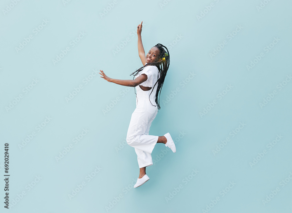 Happy woman in white casual clothes jumping against a blue wall. Young female with braids jumps outdoors. - obrazy, fototapety, plakaty 
