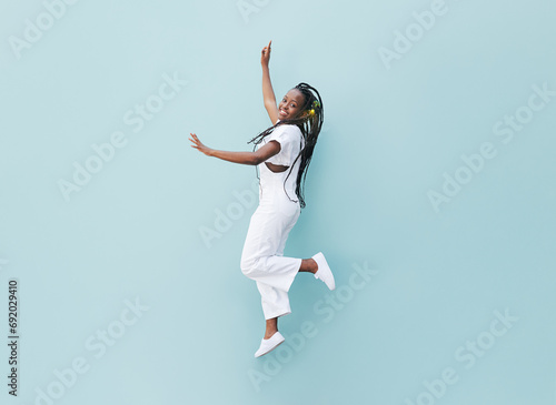 Happy woman in white casual clothes jumping against a blue wall. Young female with braids jumps outdoors.