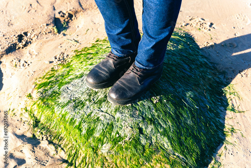 Woman's Feet in Boots and Blue Jeans Standing on Stone Covered with Green Algae