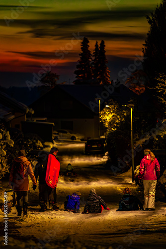 Family walking with kids on snow road over the village during sunset