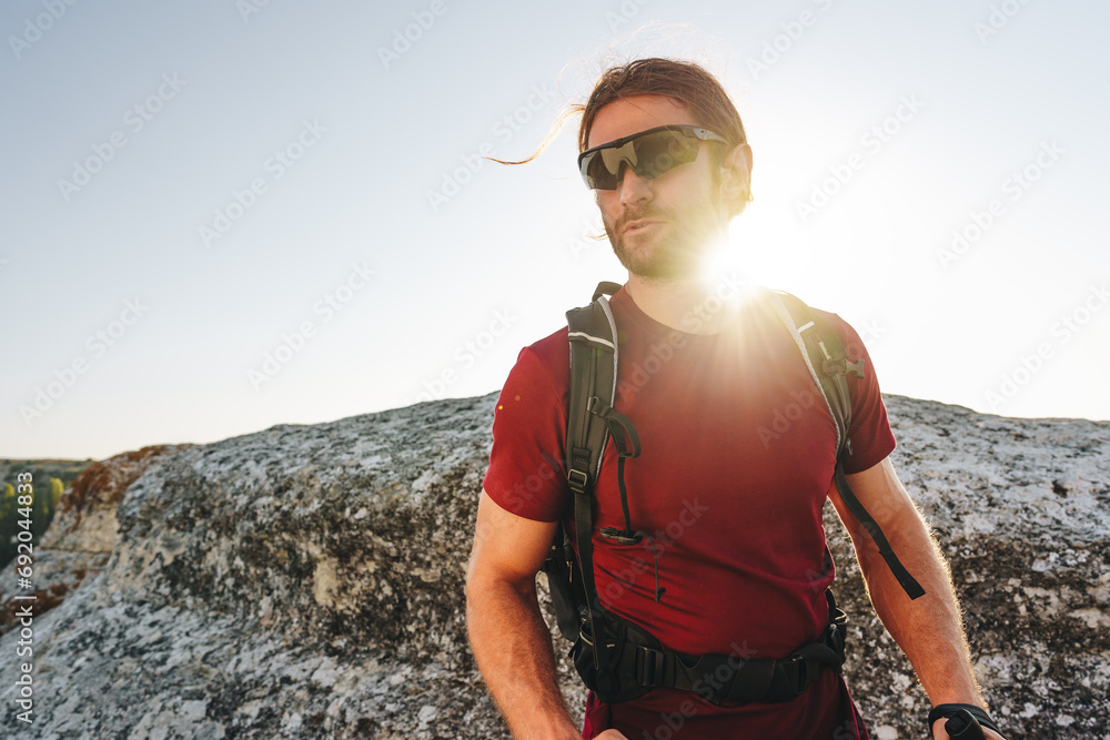 Bearded traveler with a backpack and sunglasses on the top of a mountain