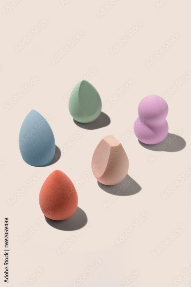 Set of colourful pastel blue, orange, biege, green and purple sponges for makeup on beige background with dark shadows. Beauty blender with different shape. Set of colourful pastel blue, orange, biege, green and purple sponges for makeup on beige background with dark shadows. Beauty blender with different shape.
