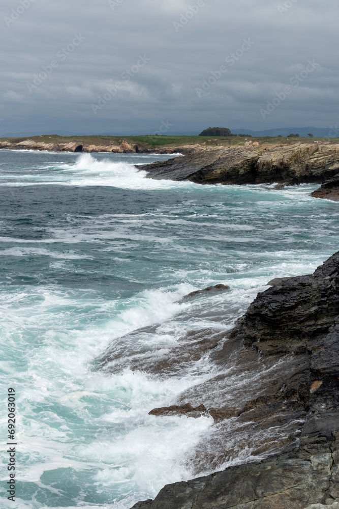 A rocky coastline with turbulent waves crashing, under a cloudy sky, exuding a moody and dramatic atmosphere A rocky coastline with turbulent waves crashing, under a cloudy sky, exuding a moody and dramatic atmosphere