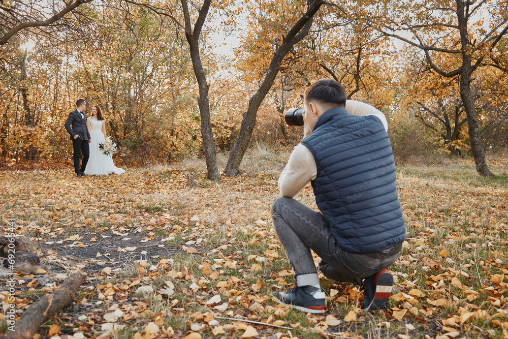 Male wedding photographer taking pictures of the bride and groom in nature in autumn Male wedding photographer taking pictures of the bride and groom in nature in autumn