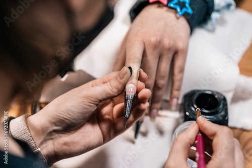 Manicure master drawing on nail of customer in studio photo