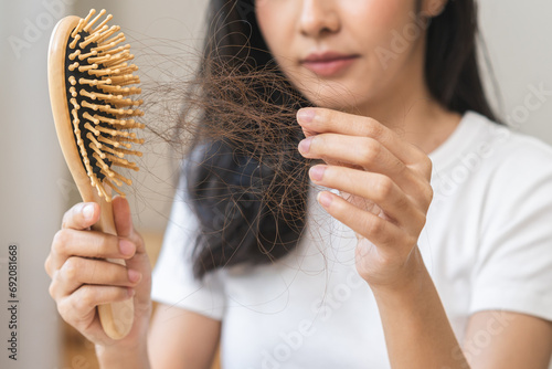 Serious asian young woman holding brush holding comb, hairbrush with fall black hair from scalp after brushing, looking on hand worry about balding. Health care, beauty treatment, hair loss problem.