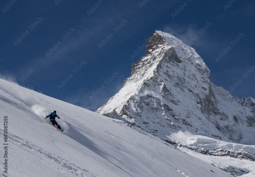 Anonymous Tourist in ski suit skiing on mountain slope against rocky mountain during vacation at Swiss Alps Anonymous Tourist in ski suit skiing on mountain slope against rocky mountain during vacation at Swiss Alps