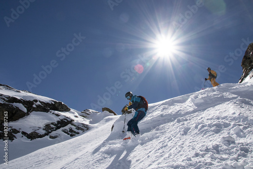 Low angle of Anonymous Tourists in ski suit skiing down on mountain slope on sunny day during vacation at Swiss Alps photo