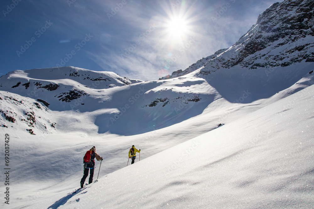 Back view of unrecognizable tourists skiing up snow-capped mountain slope under blue sky in Zermatt Back view of unrecognizable tourists skiing up snow-capped mountain slope under blue sky in Zermatt
