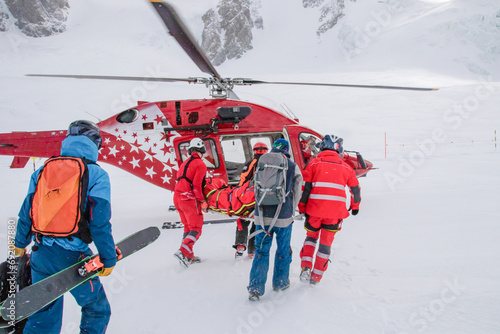 Unrecognizable Rescuers carrying injured skier to helicopter in ski area in Zermatt photo