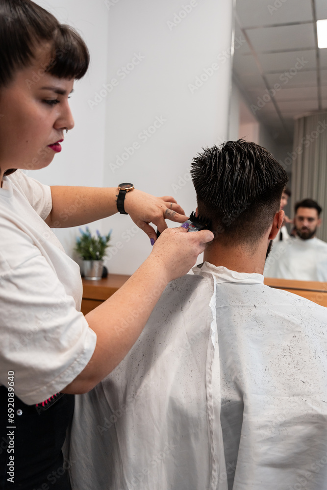 Side view of focused female hairstylist using electric trimmer on male client's hair at salon Side view of focused female hairstylist using electric trimmer on male client's hair at salon