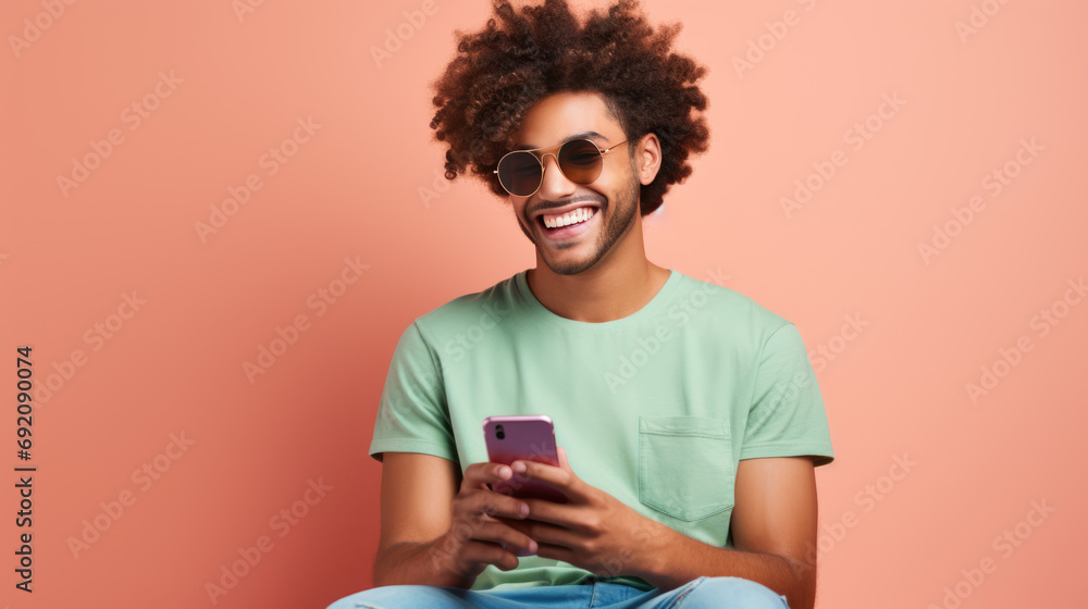 Young guy smiling holding a smartphone sitting against colored background Young guy smiling holding a smartphone sitting against colored background