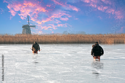 Ice sledging on a cold winterday at the windmill in the Netherlands at sunset photo