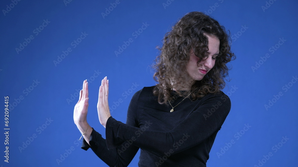 20s Female Expressing Refusal and Disgust with Hand Gesture, woman pushing away with hands sideways on blue background 20s Female Expressing Refusal and Disgust with Hand Gesture, woman pushing away with hands sideways on blue background
