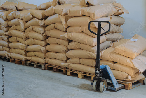 Hydraulic lifter carriage - hand pallet truck. Filled kraft paper bags on wooden pallets in warehouse room of an industrial building. photo