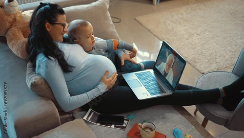 Happy pregnant mother with laptop having video call with doctor at home photo