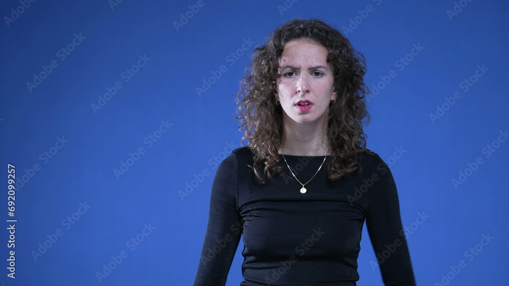 Αυτοκόλλητο Shocked woman reacting with perplexity on blue background with hands on hip, sur