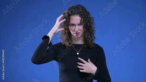 Young Woman in Shock Pointing to Herself Over Accusation signalling that accuser is crazy or wacky standing on blue background, pointing finger at herself in disbelief photo