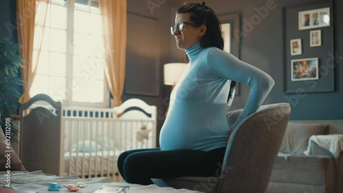 A pregnant woman feels pain in her back and feels bad sitting in an armchair at home photo