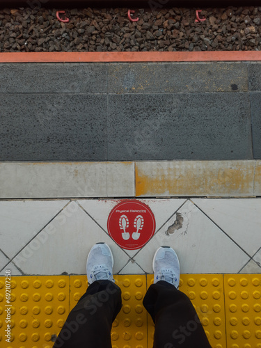 Foot passenger on the train station platform with a physical distancing sign