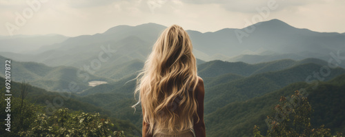 Woman with long wavy blond hairs with nature in background. Dense long blonde hair rear view