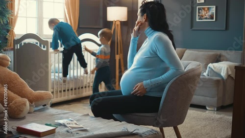 An anxious pregnant mother feels nervous and exhausted while her children play running around her photo