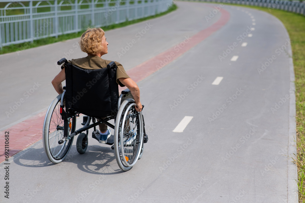 Rear view of an elderly woman in a wheelchair riding on a bike path. 