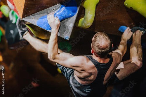 Young athletic guy in black tank top climbing climbing wall at climbing competition