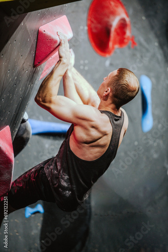 Young athletic guy in black tank top climbing climbing wall at climbing competition