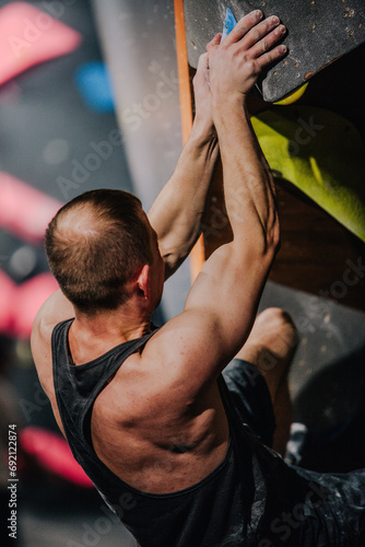 Young athletic guy in black tank top climbing climbing wall at climbing competition