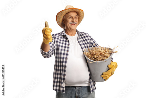Happy mature farmer holding a bucket full of hay and gesturing thumbs up