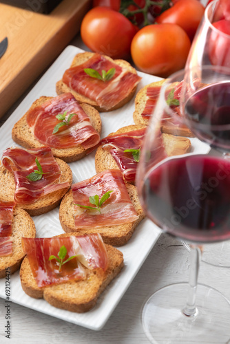 Aperitivos españoles.
Aperitivos de jamón ibérico con una copa de vino, tomates maduros 
y queso de vaca sobre fondo blanco de madera.